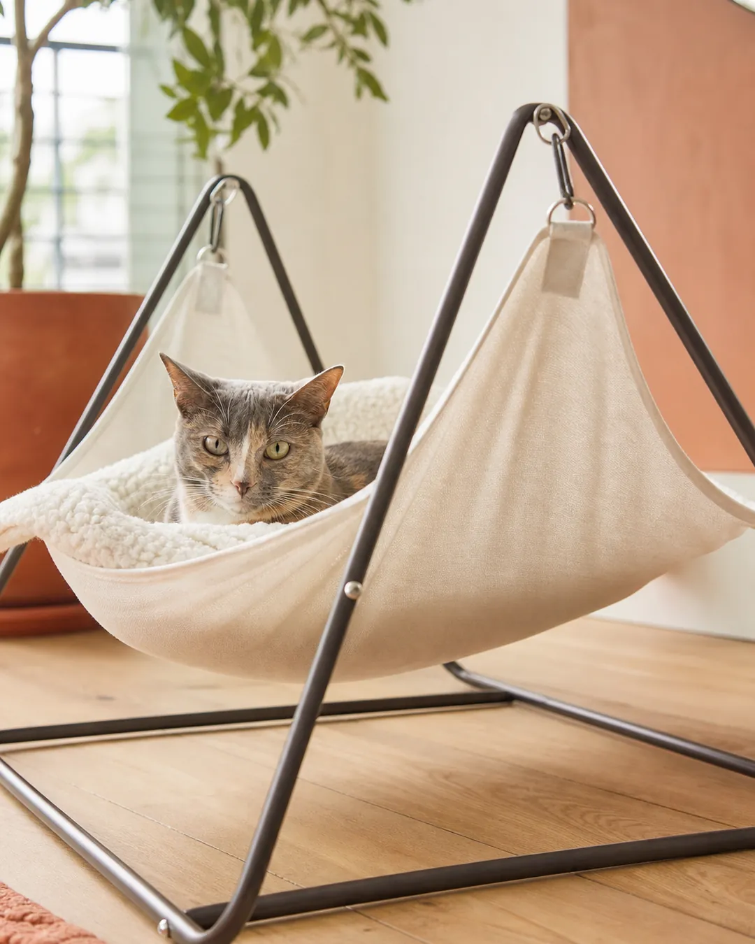 Freestanding metal frame cat hammock standing on a bare wooden floor