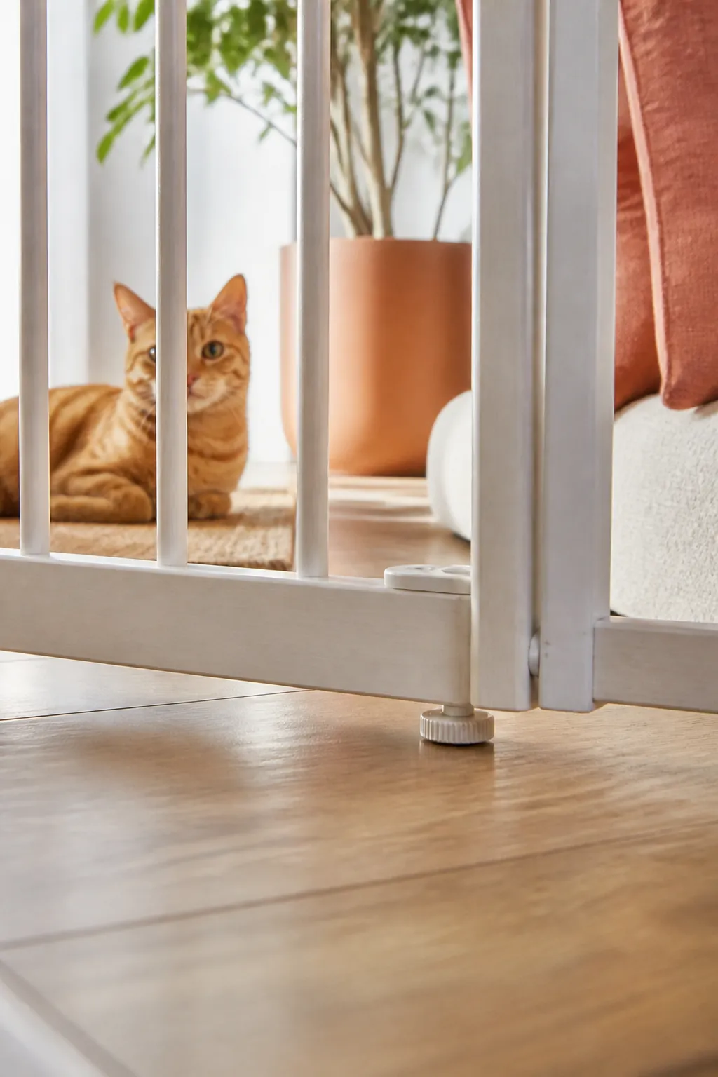 Pet gate's bottom rail and adjustable feet resting just above a hardwood floor, a narrow gap visible.